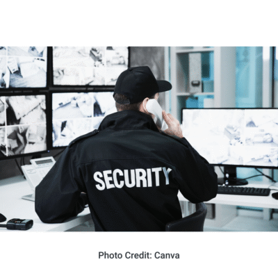 Security officer working at computer video surveillance station while talking on the phone